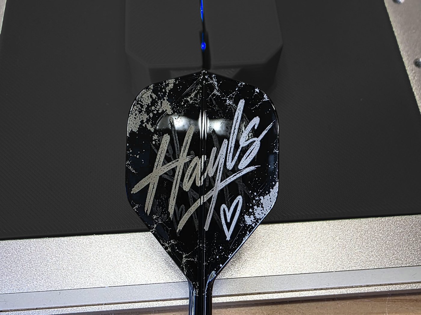 A black dart flight engraved with the name Hayls in white script and a small heart