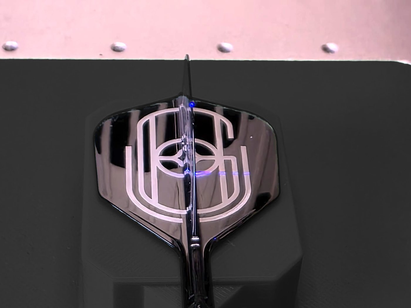 A black flight engraved in white with a monogram, sitting in the jig of the laser engraver