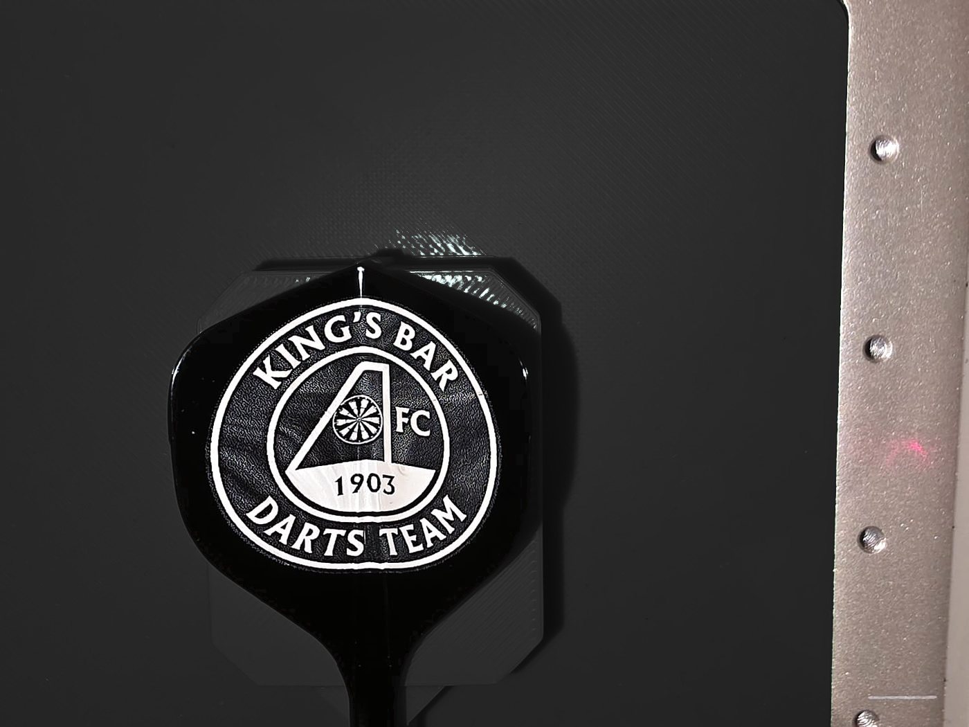 A black flight engraved with the King's Bar Darts Team crest, sitting in the laser jig