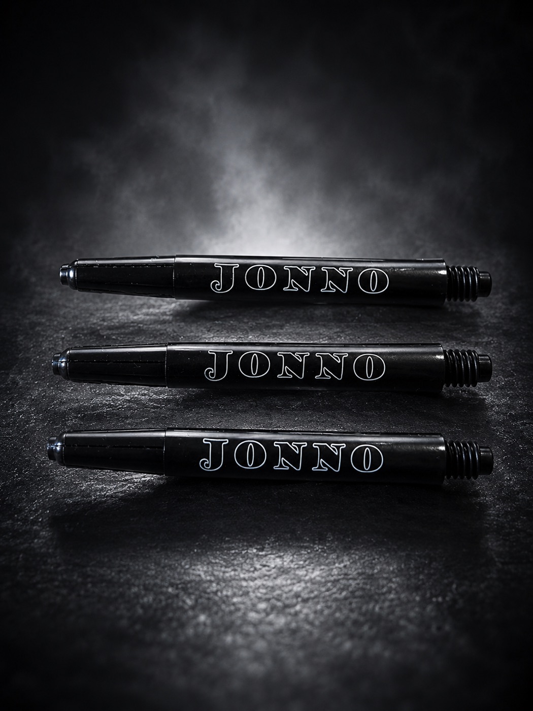 Three black dart shafts laid in a row, each engraved in white with the same name